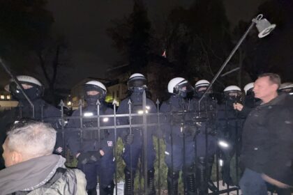 Policjanci za ogrodzeniem przed siedzibą Trybunału Konstytucyjnego nocą. Zdjęcie ilustrujące okoliczności wydarzeń.