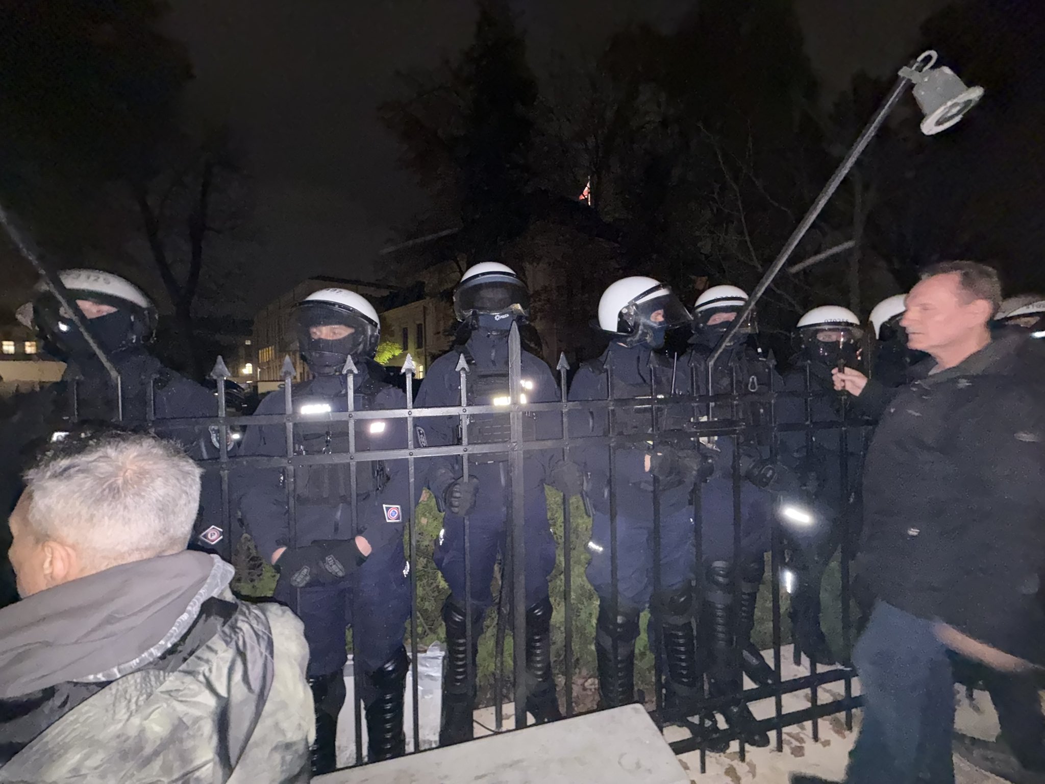 Policjanci za ogrodzeniem przed siedzibą Trybunału Konstytucyjnego nocą. Zdjęcie ilustrujące okoliczności wydarzeń.